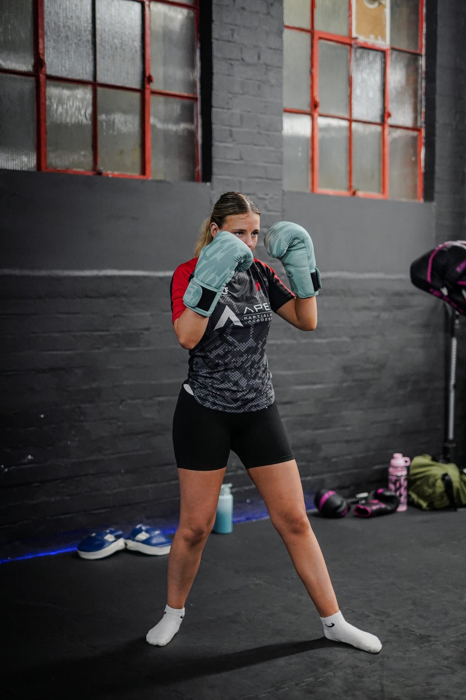 Adult Apex member in fight stance against the academy&rsquo;s industrial backdrop.