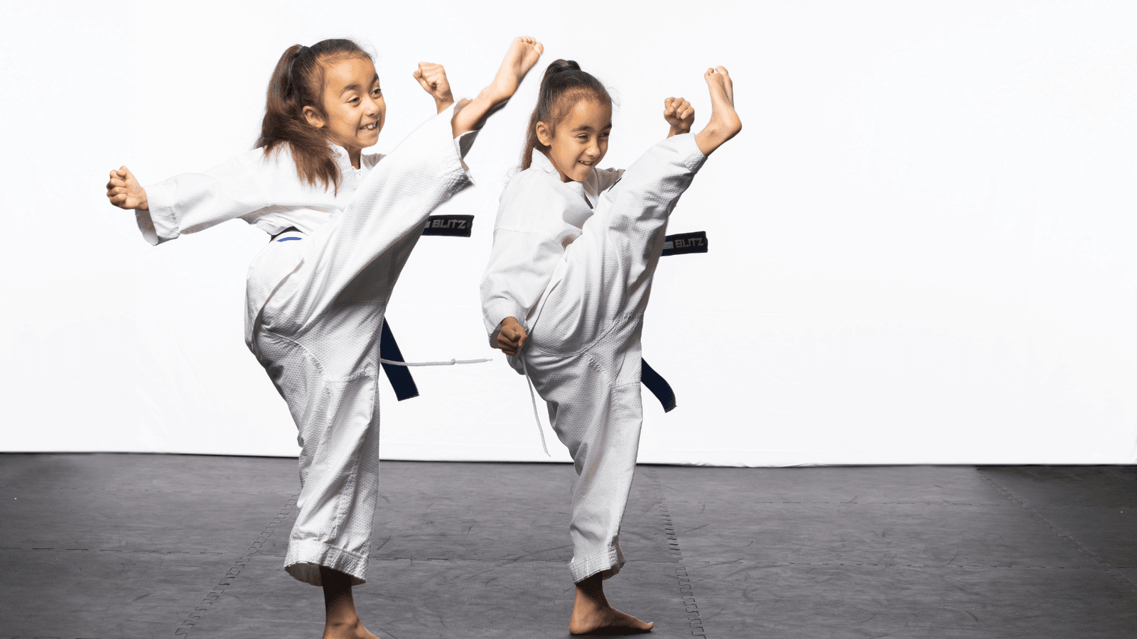 Two young children in white gi having fun on the mats.