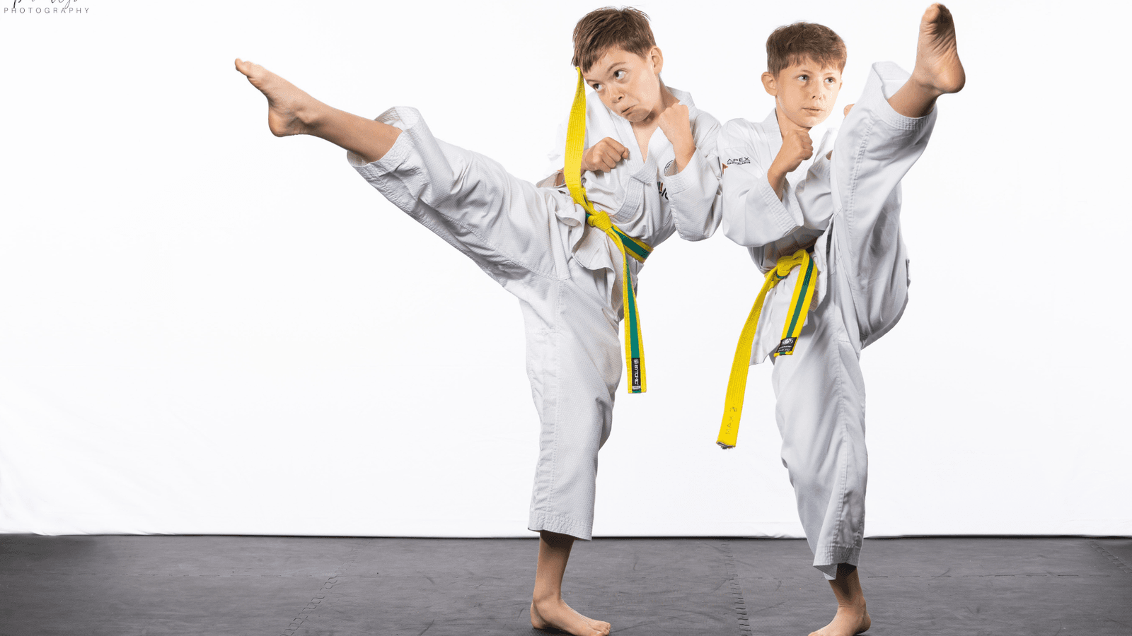 Two junior students in white gi performing high kicks.